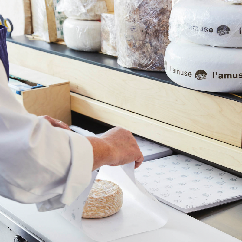 Person wrapping a piece of cheese at a cheese shop counter.