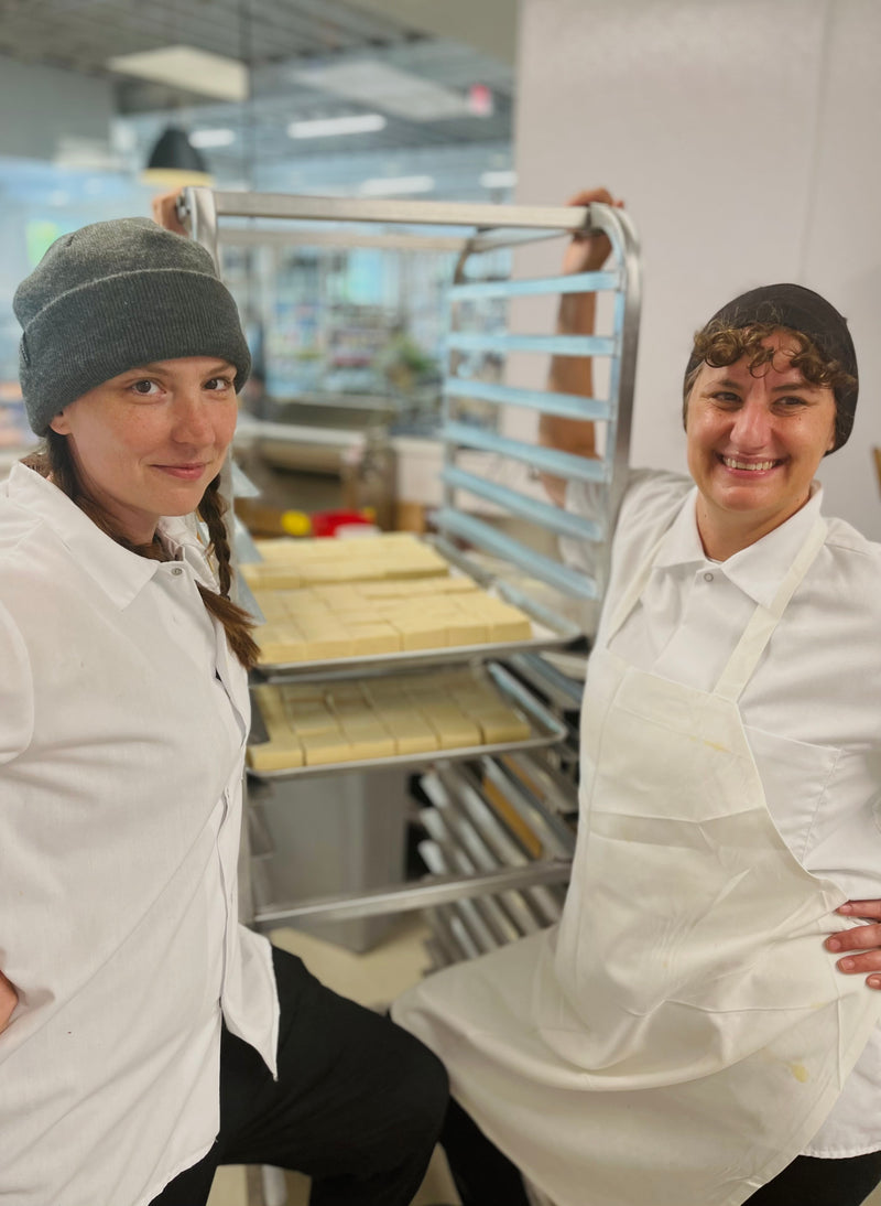 Two people in a bakery kitchen posing with a tray rack.
