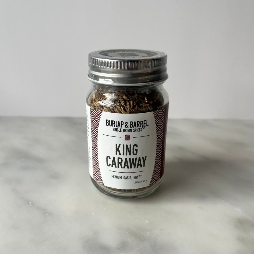 A jar of caraway seeds on a marble surface.