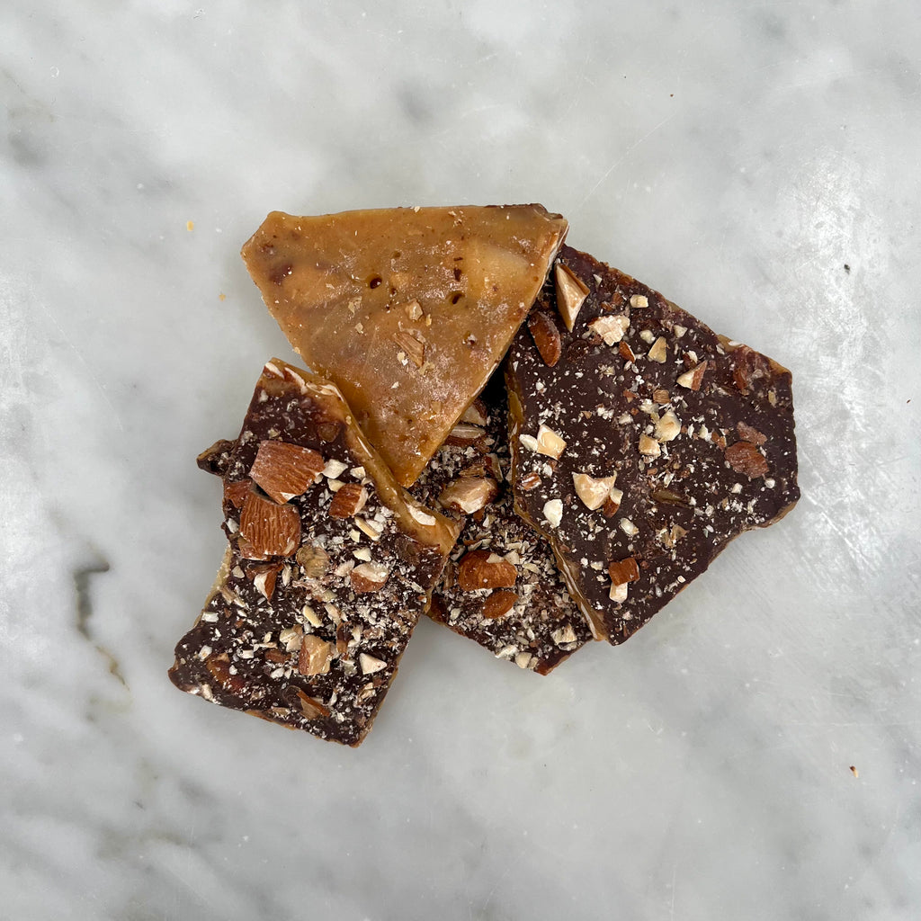 Three pieces of nut-topped chocolate bark on a marble surface.