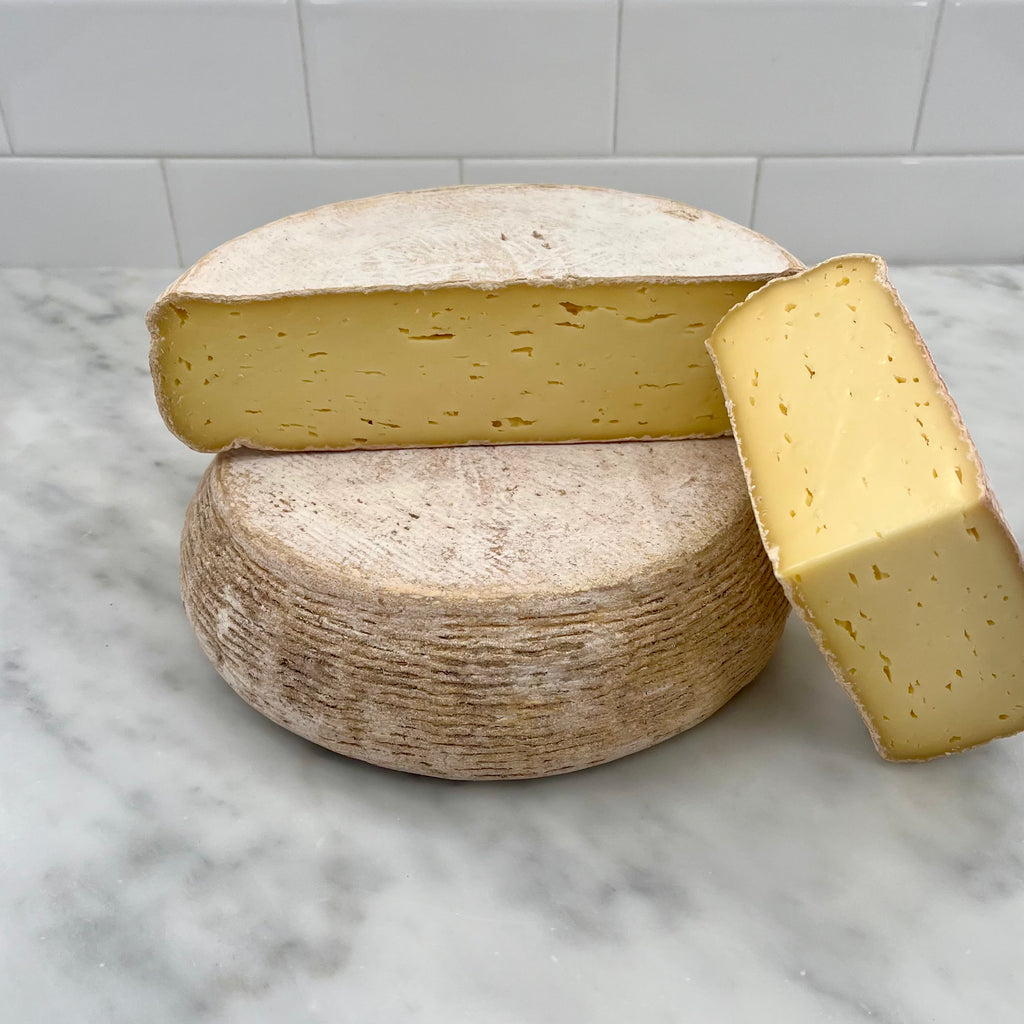 Two wheels of cheese on a marble surface, one with a wedge cut out.