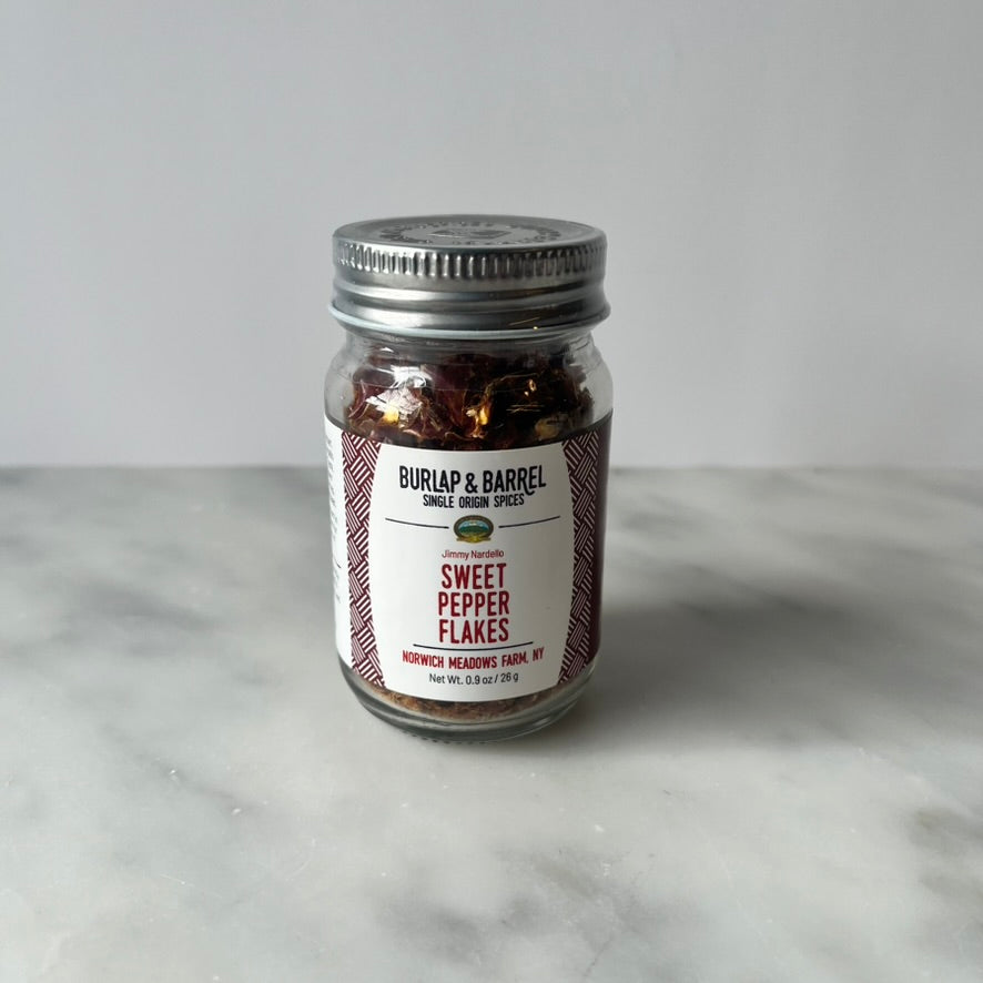 A jar of sweet pepper flakes on a marble surface.