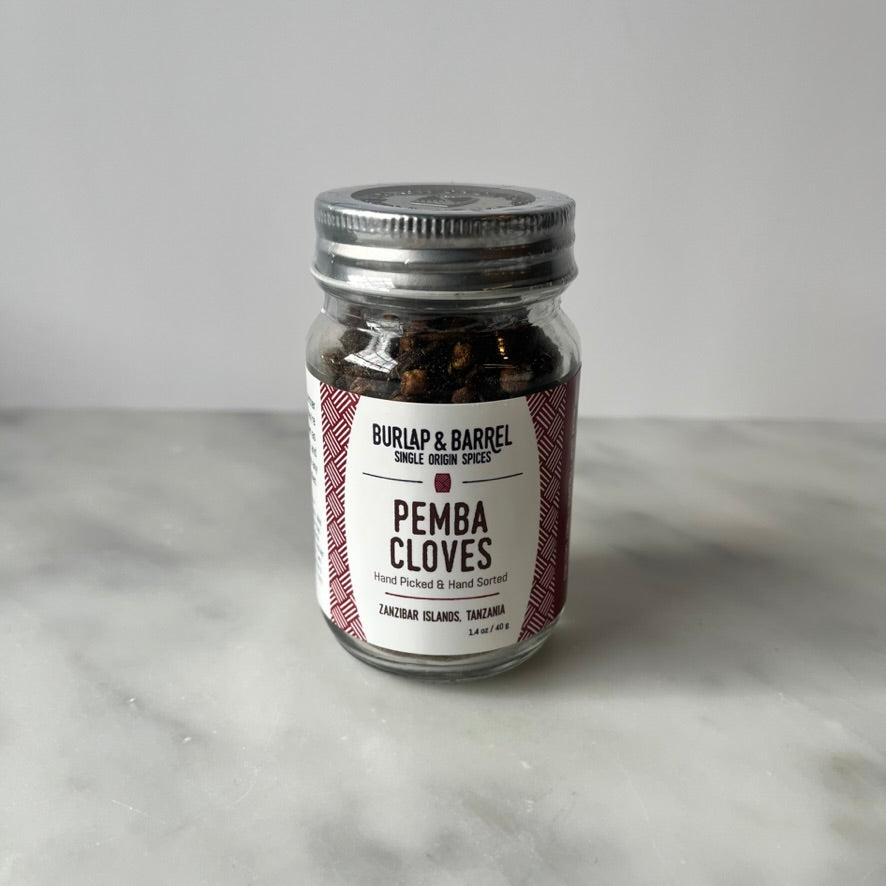 Glass jar of cloves on a marble surface.
