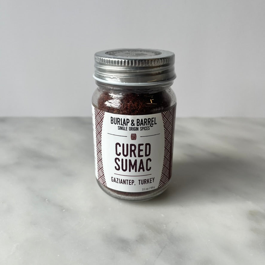 Jar of cured sumac on a marble surface.