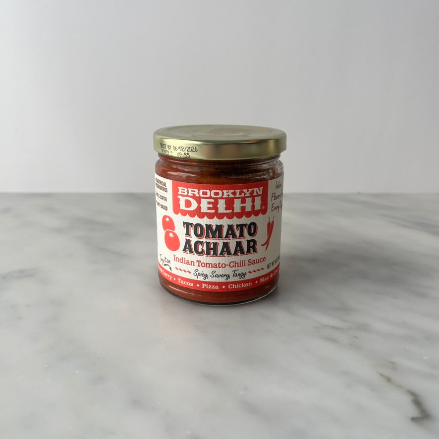 A jar of tomato achaar on a marble countertop.