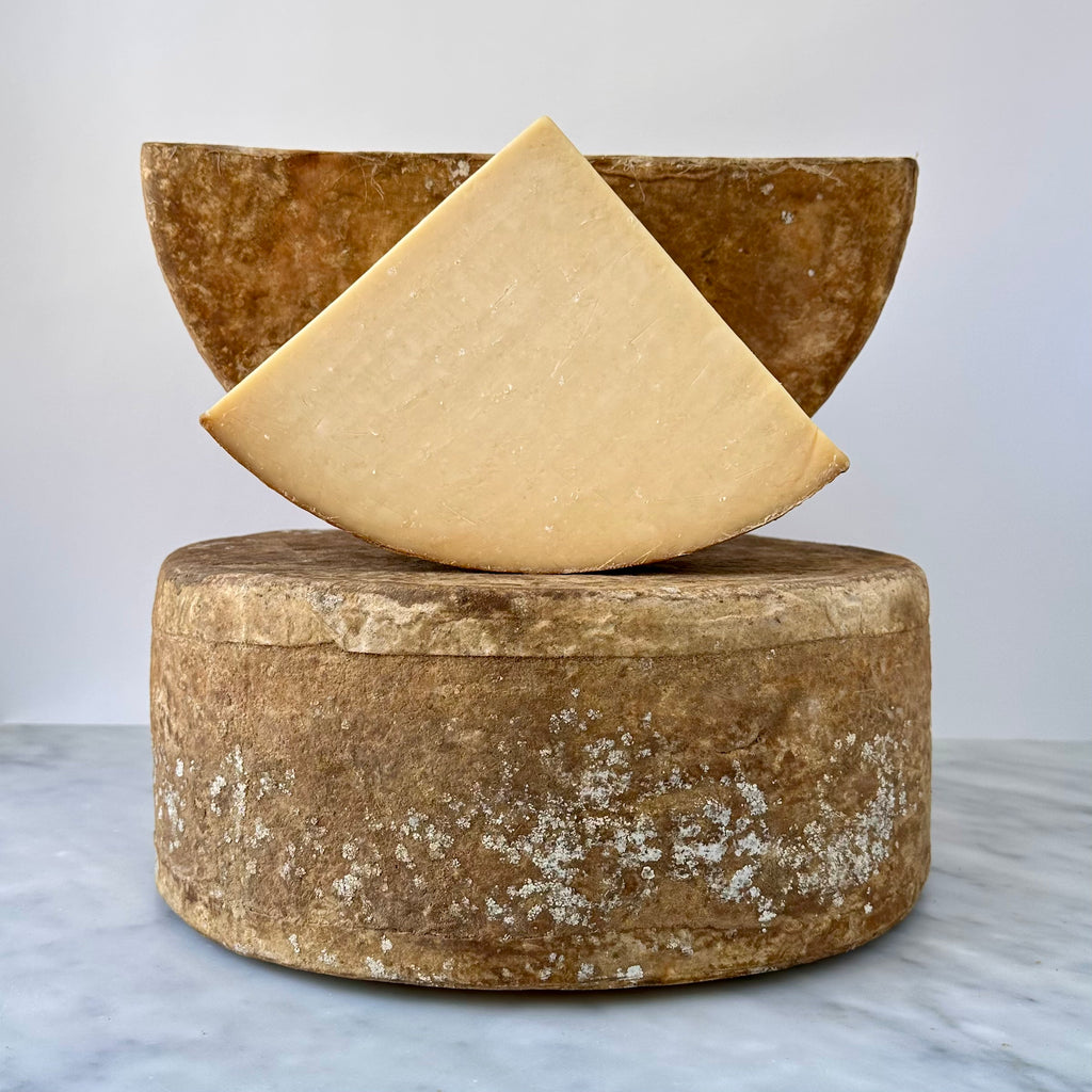 A wedge and wheel of cheese on a table.