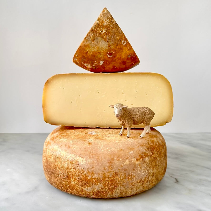 Stacked cheeses with a sheep figurine.