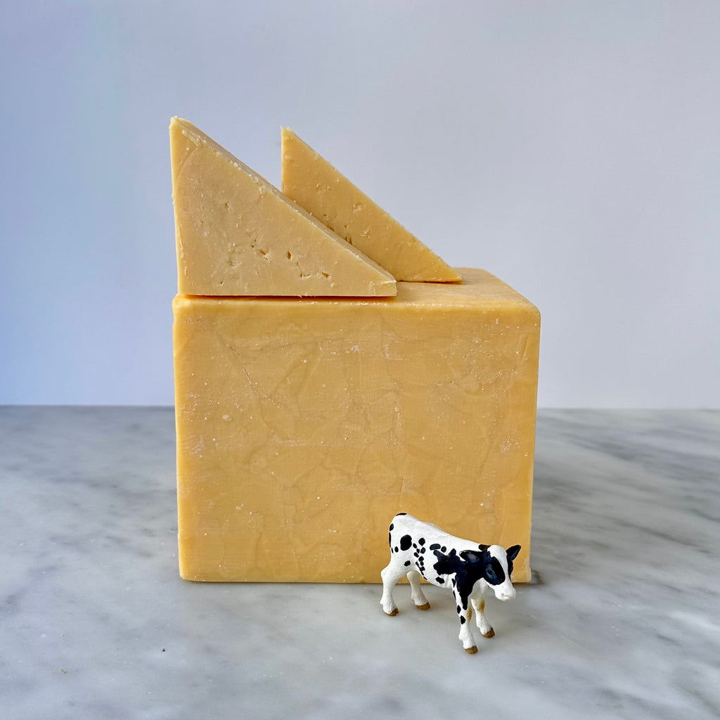 A block of cheese with slices alongside a small cow figurine.