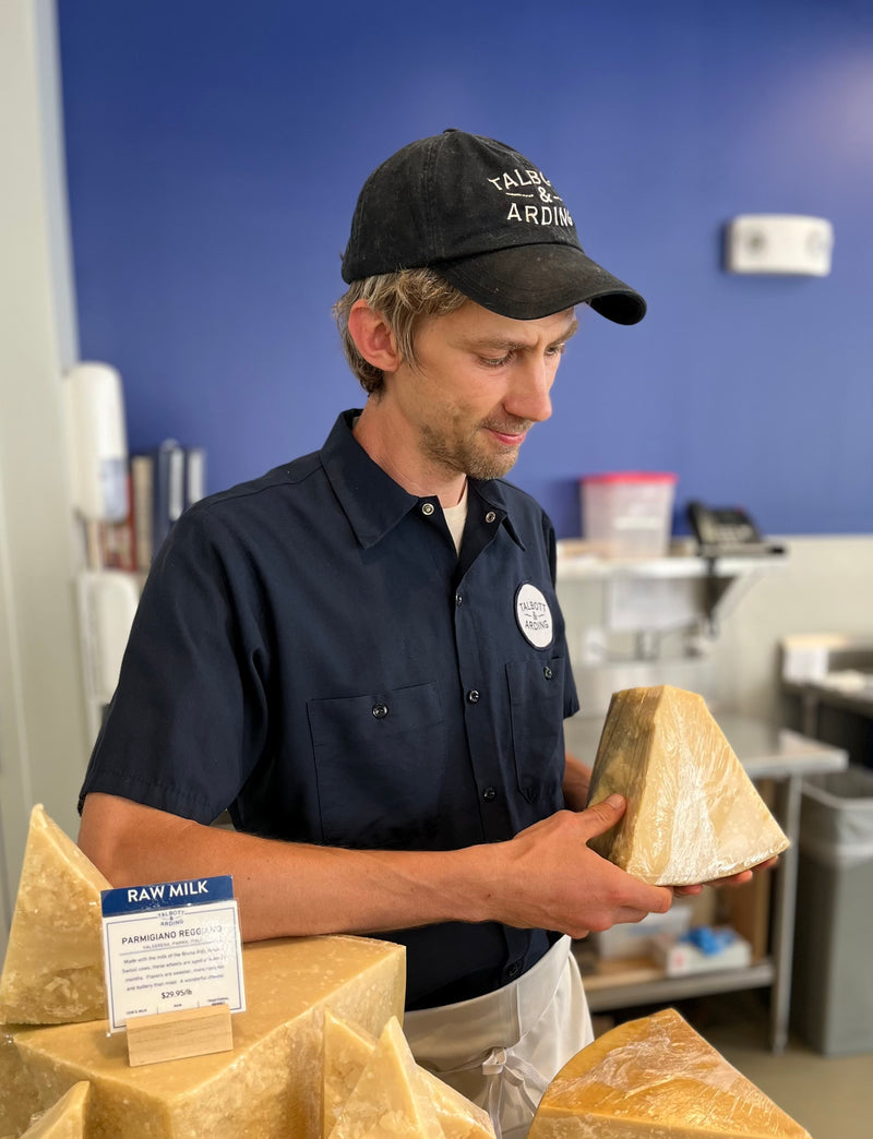 A person inspecting a piece of cheese at a cheese shop.