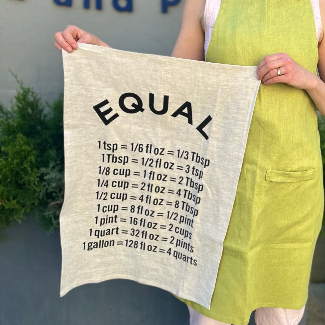 Home cook holding tea towel printed with common unit conversions used for cooking and baking.