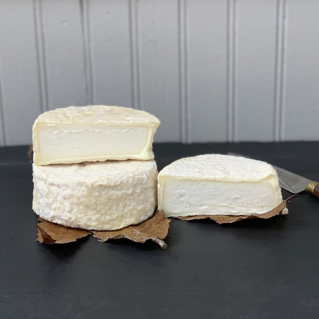 Two wheels of soft cheese on a black surface with one cut in half.